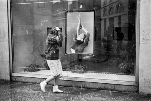 Woman on sidewalk passing a photo of a model in gallery window. Prague, Czech Republic.