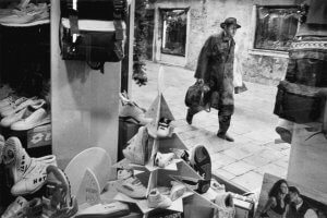 A conservatively dressed man walks past an athletic shoe window display. Venice, Italy.